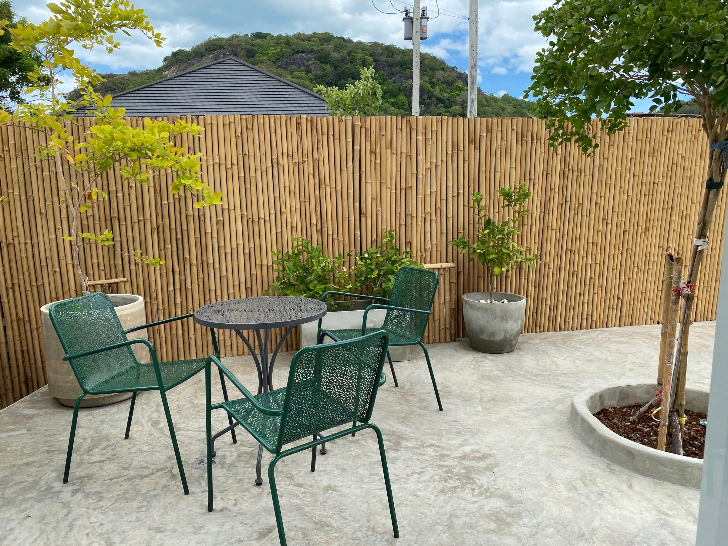 Courtyard with green bistro chairs, a bamboo fence and a hill behind