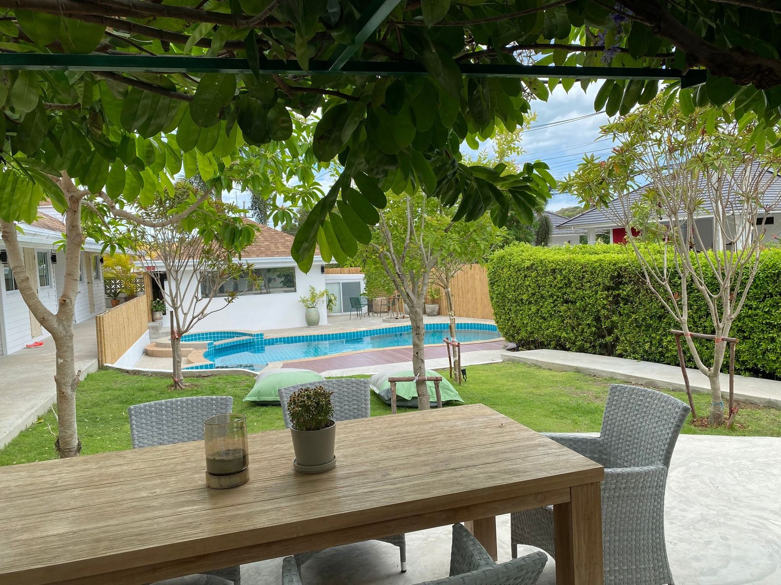 Garden dining table under shade trees beside the lawn and swimming pool at The White Room, Hua Hin