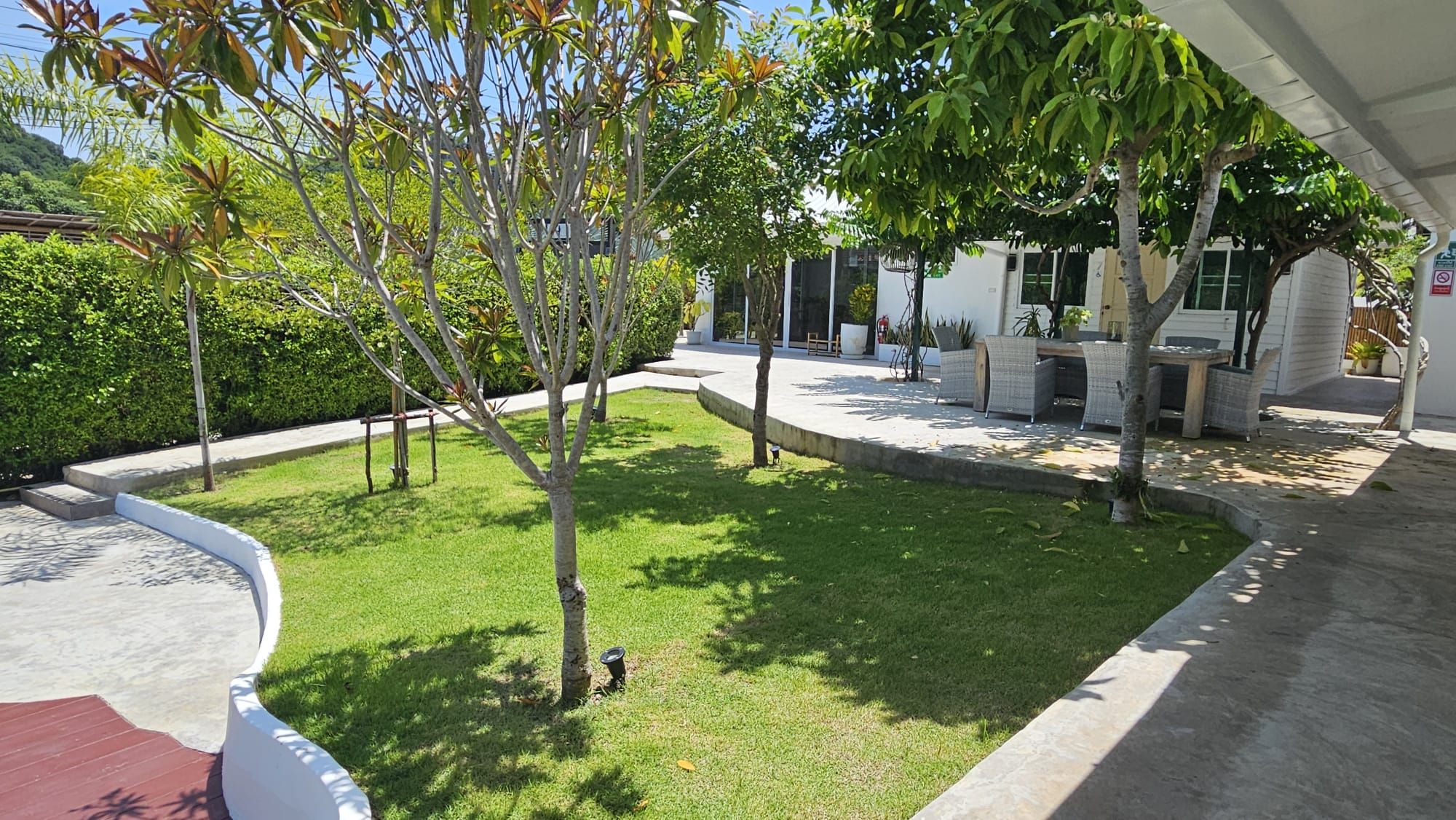 Sunny lawn with young shade trees and a curving path leading to the outdoor dining table and bungalows at The White Room