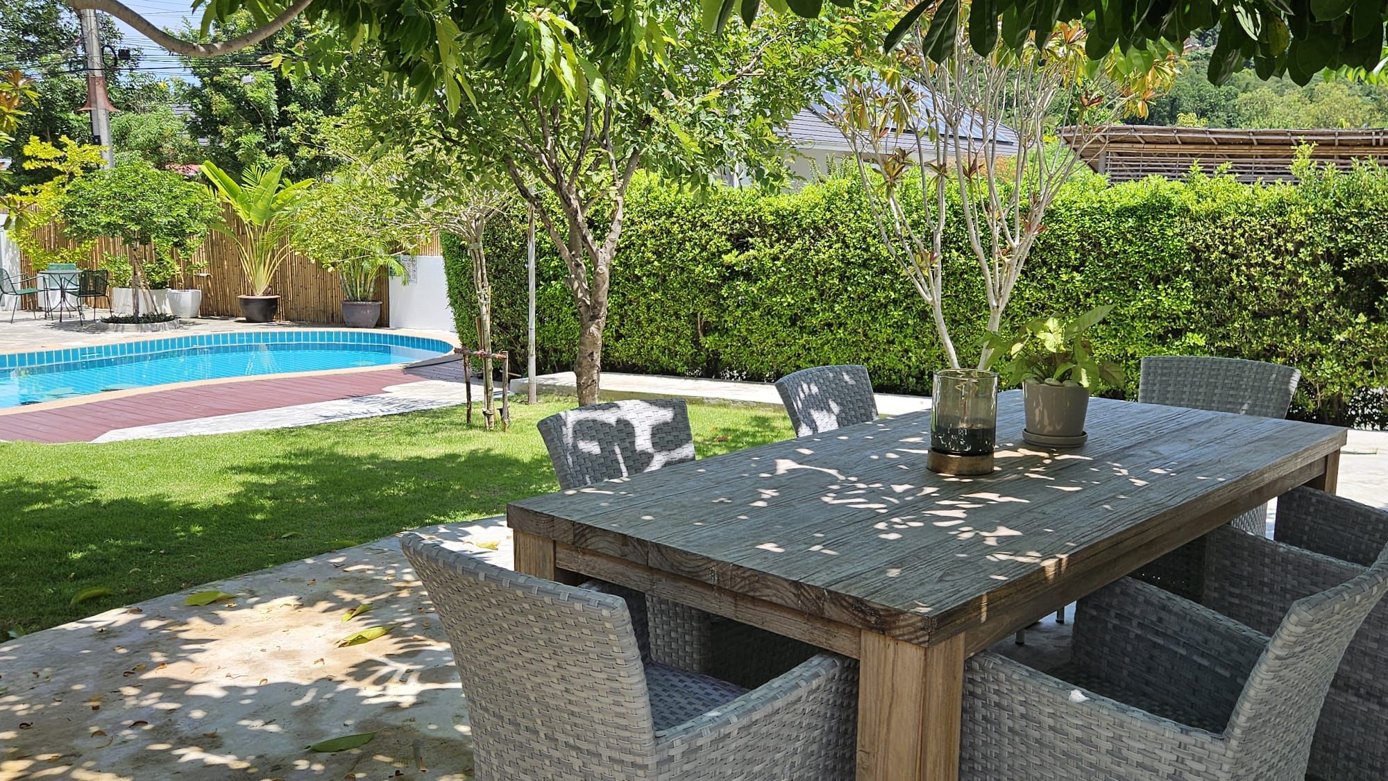 Garden dining table on the lawn beside the swimming pool, with trees and a green hedge, at The White Room