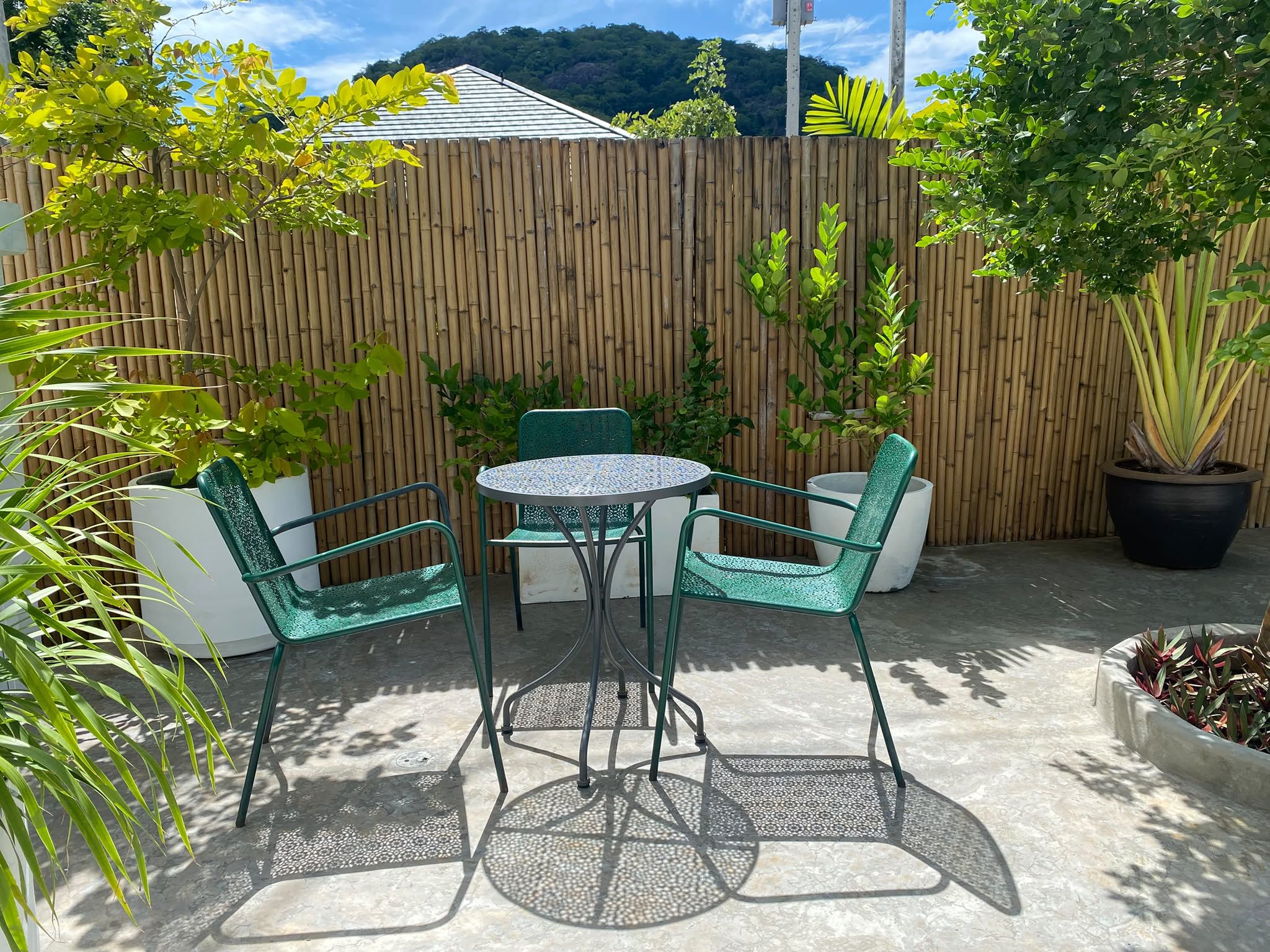 Private courtyard with green bistro chairs and a mountain behind the bamboo fence